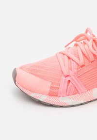 Scarpa sportiva rosa con tomaia in mesh testurizzato, lacci piatti, suola in gomma e accenti a strisce sulla suola. Design della punta arrotondata.