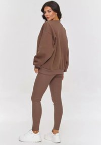Brązowy, oversized sweatshirt oraz teksturowane brązowe legginsy, połączone z białymi, platformowymi sneakersami, prezentujące swobodny, luźny wygląd.