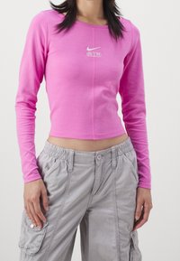 Figurpassande långärmad topp i knallrosa bomull, med en mittsöm och en vit Nike AIR-logotyp. Kombinerad med grå cargobyxor.