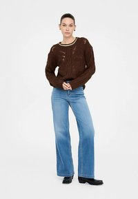 Barna kötött pulóver áttört mintával, világoskék bő szárú farmerrel és fekete bokacsizmával párosítva.