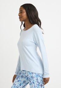 Ljusblå långärmad skjorta med rund halsringning, som har en avslappnad passform och mjuk textur, tillsammans med flerfärgade mönstrade leggings.