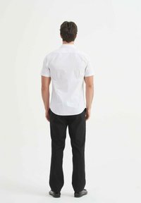 Chemise blanche à manches courtes, pantalon noir, design uni, vue de dos, tissu lisse, coupe droite, sans motifs, col simple, chaussures noires.