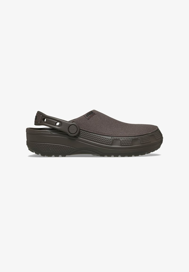 Brauner Slip-On-Pantolette mit strukturierter Oberfläche, verstellbarem Fersenriemen und dicker, profillaufsohlenartiger Sohle, die für den Alltag konzipiert ist.