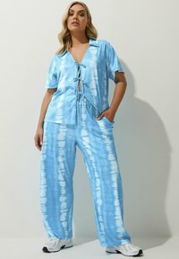 Jumpsuit blu tie-dye con maniche corte, scollatura a V profonda, elastico regolabile davanti e pantaloni a gamba larga. Presenta un tessuto strutturato a coste.