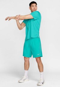 Conjunto atlético turquesa composto por uma t-shirt de manga curta que afasta a humidade e calções combinando com cintura elástica e logótipo da Nike.