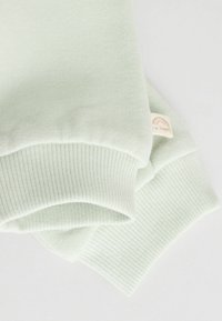 Lysegrøn sweatermanchetter lavet af blødt stof, prydet med ribbet tekstur og et lille mærke med et regnbuedesign.