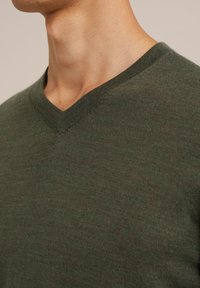 Grön v-ringad tröja i mjukt material med en slät yta och subtil sömnad vid halsringningen, som framhäver en figurnära design.