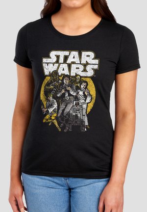Woman wearing black Star Wars t-shirt featuring key characters and droid with large vintage yellow circle background.