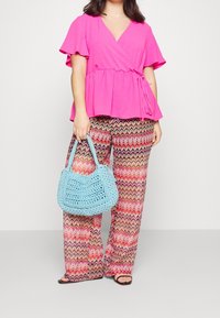 Světlá růžová zavinovací blůzka s volánovými rukávy, zkombinovaná s barevnými širokými kalhotami se vzorem cik-cak a texturovanou světle modrou háčkovanou kabelkou.