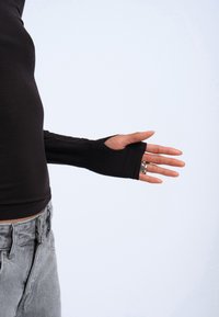 Black long-sleeve top with thumb hole, stretchy fabric, fitted design, paired with light gray high-waisted jeans. Hand with a ring visible.