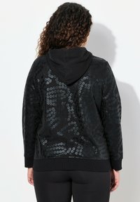 Sweat à capuche en polaire noire avec un motif texturé de sequins circulaires brillants. Dispose d'une capuche avec cordon de serrage et de poignets et d'un ourlet côtelés.