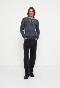 Donkerblauwe gebreide trui met een ritssluiting bij de kraag, gecombineerd met zwarte broek met wijde pijpen en zwarte chunky schoenen. Glad materiaal, casual pasvorm.