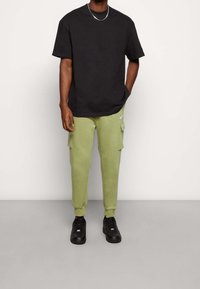 Černé bavlněné tričko s krátkými rukávy, doplněné světle zelenými cargo tepláky s bočními kapsami a černými teniskami.