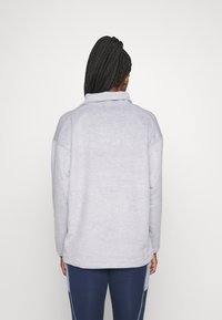 Pullover de fleece cinza com gola alta, ombros caídos e textura suave. A parte traseira apresenta um design simples e clean, sem adornos.