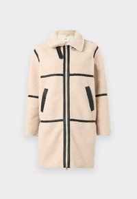 Manteau sherpa beige avec bordure noire, fermeture éclair à l'avant, deux poches latérales et un col, conçu pour temps froid.