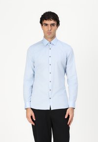 Lyseblå langermet skjorte laget av bomull. Har standard krage, frontlukking med brune knapper, og design med vanlig passform.