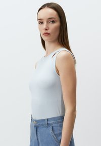 Canotta blu chiaro a costine con dettagli a spalla scoperta, abbinata a jeans a vita alta blu chiaro. Tessuto morbido e design aderente.