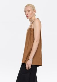 Top marrone senza maniche con una vestibilità ampia e spalline intrecciate. Realizzato in un tessuto morbido, presenta un design pulito e minimalista.