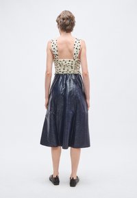 Rochia are un design fără mâneci, cu partea superioară modelată în crem și puncte negre, trecând într-o fustă lucioasă, albastru închis, până la genunchi.