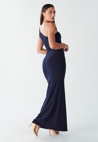 Tumši zila vakarkleita ar vienu plecu, ar pieguļošu augšdaļu un plūstošu svārku. Izgatavota no gludas, elastīgas auduma. Valkāta ar bēša krāsas papēžiem.