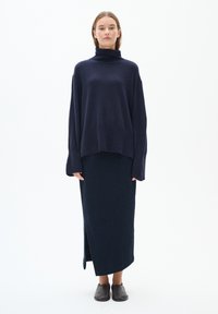 Mornarsko pulover s turtle neck iz širokega kroja in dolgimi rokavi, ujemajoč z dolgim mornarskim krilom z bočno režo. Rjave ravne čevlje.