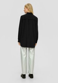 Schwarzes Langarmshirt mit Rückenpasse, kombiniert mit glänzenden silbernen weit geschnittenen Hosen und klobigen schwarzen Plateauschuhen.