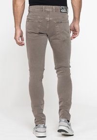 Jeans slim fit marroni con una texture liscia, design a cinque tasche, cuciture in contrasto e un piccolo marchio nella parte posteriore della cintura.
