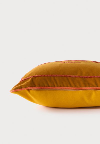 Oreiller rectangulaire jaune moutarde avec passepoil orange-rouge et détails brodés, vu de profil sur fond blanc.