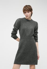 Vestido cinza de malha com decote redondo, punhos canelados e corpete justo que transita para uma bainha rodada. O tecido texturizado acrescenta profundidade.