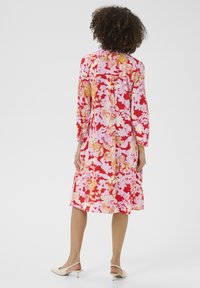 Lillelillekgaane, kus on punased, roosad ja kuldsed toonid, pikkade varrukatega, vormitud bodice'ga ja flared seelikuosa, mis ulatub kuni pahkluuni.