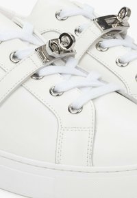 Witte leren sneakers met zilverkleurige hardware, ronde metalen oogjes, platte witte veters en een gestructureerde rubberen zool.