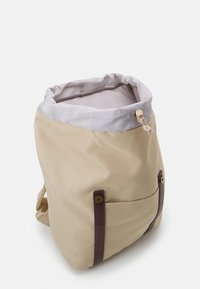 Sac à dos en toile beige avec une doublure en tissu rayé, une fermeture à cordon et des accents en cuir marron. Comprend une poche latérale avec un détail de bouton.