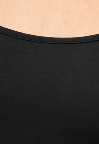 Κοντινό πλάνο του άνω μέρους του στήθους και του λαιμού ενός ατόμου που φοράει ένα μαύρο τοπ από ριμπ ύφασμα με στρογγυλή λαιμόκοψη.