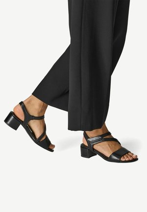 Black leather sandals with a block heel and crisscross straps. Open-toed design and smooth finish, complemented by a sleek silhouette.