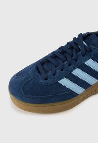 Ténis de camurça azul com três riscas azul claro, sola de borracha texturizada e atacadores a condizer. Biqueira arredondada e colarinho acolchoado.