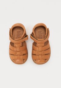 Sandales en cuir marron avec un design à lanières, sangle de cheville réglable, texture lisse et bout ouvert pour une meilleure ventilation.
