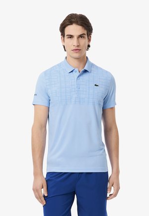 Polo di colore azzurro chiaro con un motivo a griglia testurizzato nella parte superiore, dotato di un colletto a due bottoni e un piccolo logo verde sul petto.