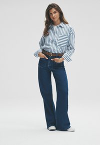 Gestreiftes blau-weißes Button-Up-Hemd mit einer Brusttasche, kombiniert mit hochtaillierten, dunkelblauen Schlagjeans und einem braunen Gürtel.