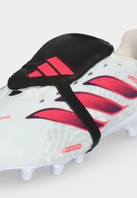 Λευκό και ροζ ποδοσφαιρικό παπούτσι Adidas με μαύρο κάλυμμα κορδονιών που φέρει κόκκινο λογότυπο Adidas σε σόλα από τεχνητό χορτάρι.