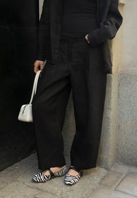 Črna lanena obleka z oversize hlačami in krojenim jopičem. Črno-beli črtasti balerinki in mala bela torbica.