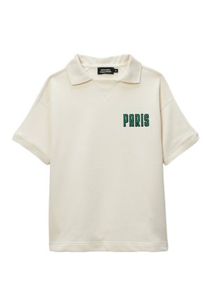 Polo-shirt à manches courtes crème avec un col en V et le texte "PARIS" brodé en vert sur la poitrine gauche. Tissu doux avec une coupe décontractée.