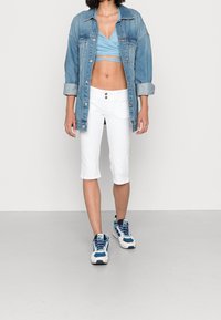 Oversized džínová bunda, světle modrý crop top, bílé kalhoty po kolena a tenisky s modrými detaily. Klíčové vlastnosti: kontrast barev a pohodlný střih.