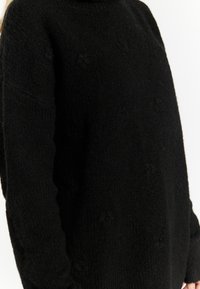 Maglione nero in maglia testurizzata con colletto alto, caratterizzato da una vestibilità ampia e da sottili motivi in rilievo sul tessuto.