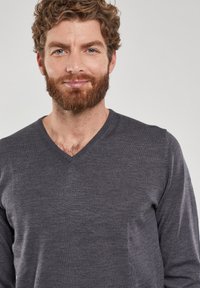 Pull en v gris foncé en tricot doux, avec une coupe décontractée et une texture visible présentant un subtil éclat.