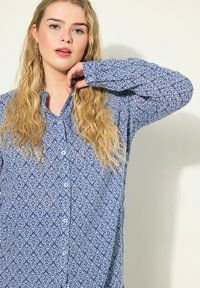 Camicia a maniche lunghe con bottoni di colore blu e con un motivo geometrico bianco. Presenta un colletto e una vestibilità comoda, realizzata in tessuto testurizzato.