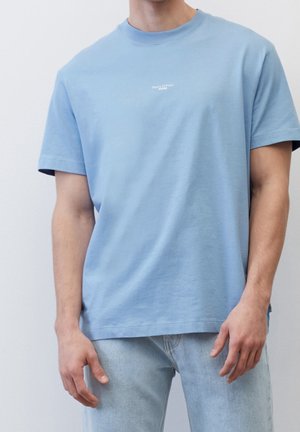 T-shirt en coton bleu clair avec un col rond et des manches courtes. Présente un petit logo blanc sur la poitrine et un design à coupe décontractée.