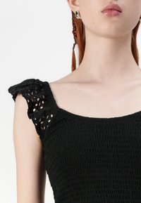 Crna smock bluzica s kvadratnim izrezom i rukavima na pruge s čipkastim detaljima. Glatka tekstura tkanine.