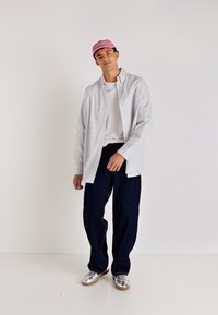 Camisa de cuadros azul claro y blanca sobre una camiseta blanca, combinada con pantalones de pierna ancha azul oscuro y una gorra rosa. Unos zapatos plateados completan el look.