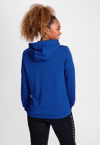 Felpa blu royal con finitura testurizzata, dotata di cappuccio con cordoncino, maniche lunghe e dettagli neri sulle spalle. Leggings neri con un motivo laterale.