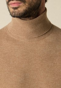 Brauner, gerippter Rollkragenpullover aus weichem Strickstoff. Nahaufnahme, die Textur und das Kragen-Design zeigt. Hat eine enge Passform.